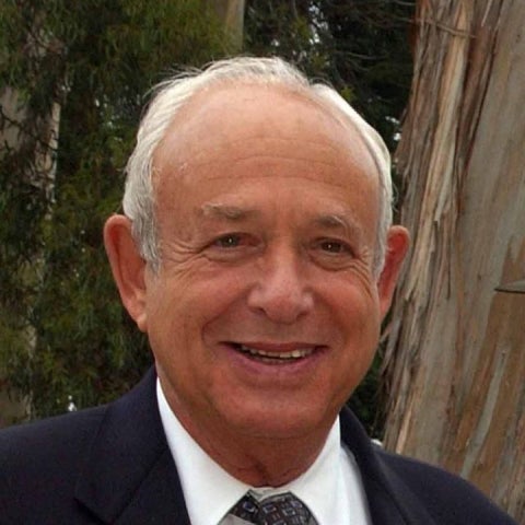 Daniel E. Morse smiles in front of a eucalpytus wears a dark suit with a white shirt