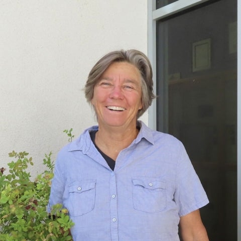 Lisa Stratton stands next to a plant, wearing a blue button-up shirt