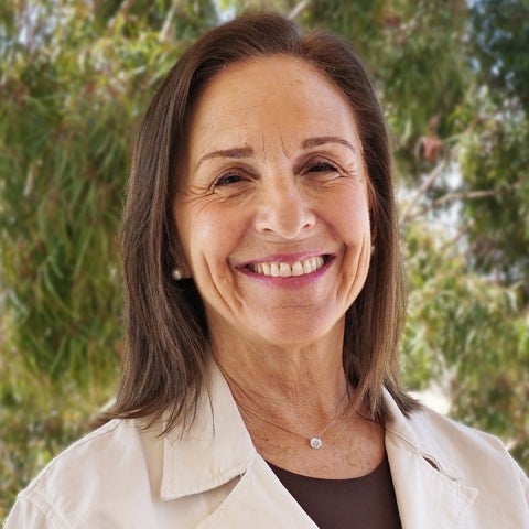 Susan Derwin smiles outside wearing a cream-colored coat over a burgandy top