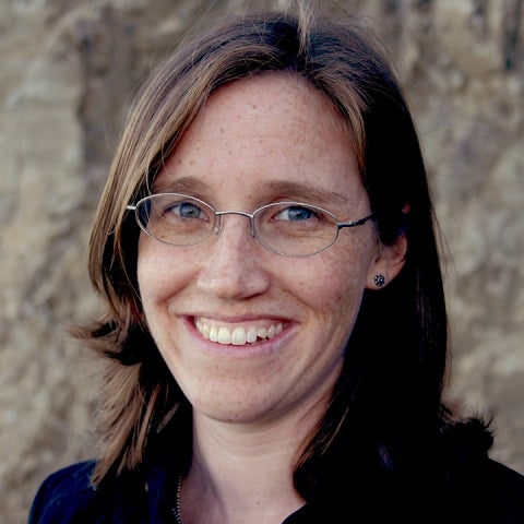 Sarah Anderson stands in front of a bluff wall wearing glasses and a dark jacket